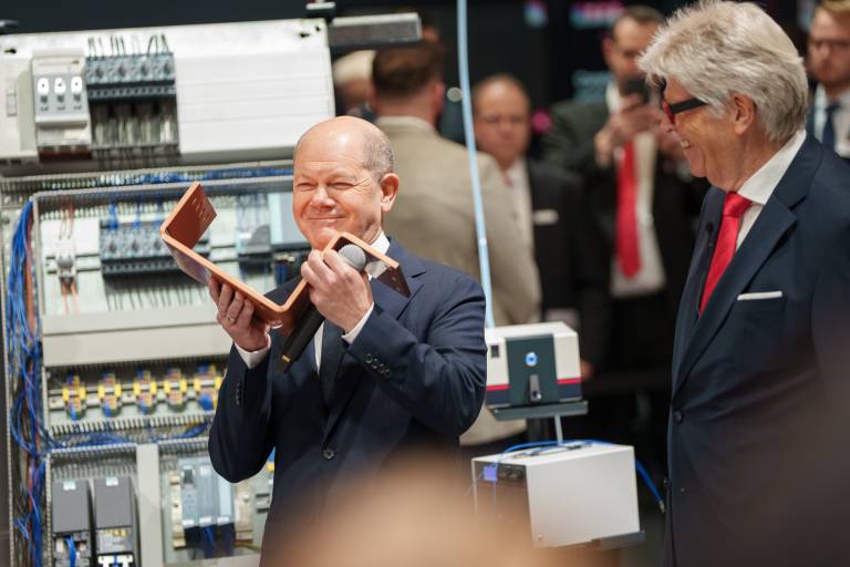 Der deutsche Bundeskanzler Olaf Scholz inspiziert im Beisein von Prof. Friedhelm Loh, Inhaber und Vorstandsvorsitzender der Friedhelm Loh Group, eine Kupferschiene für Stromverteilung.
